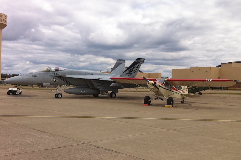 Piper Cub parked next to military jet